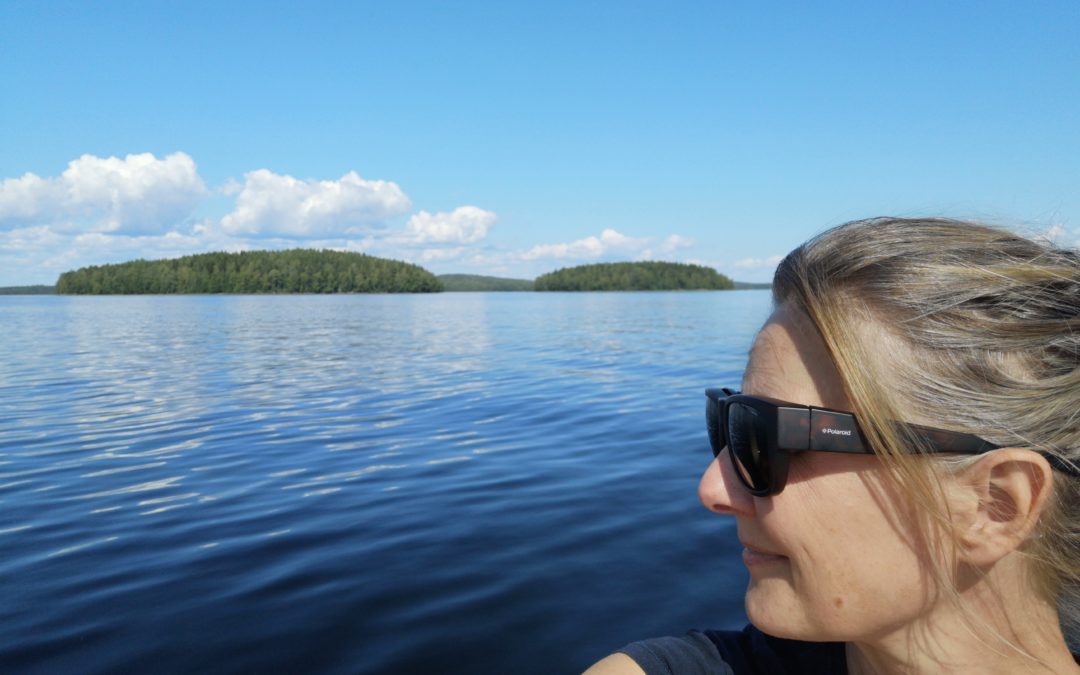 Riika Kivelä järvellä Päijänteellä. Hän katselee aurinkolasit päässään järvelle. Taustalla saaria ja kumpupilviä.