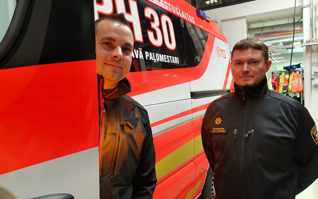 Ambulanssin vieressä seisoo kaksi miestä. Ambulanssissa teksti PH30 päivystävä palomestari.