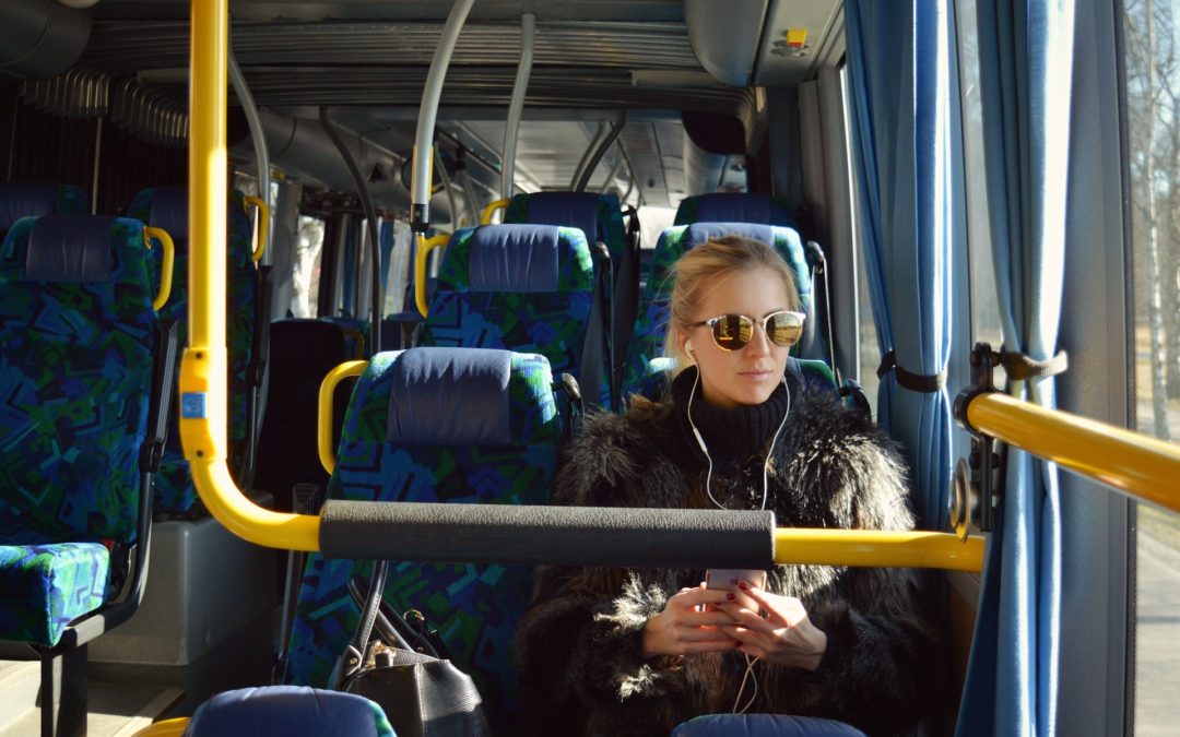 Nuori nainen istuu linja-autossa. Hänellä on aurinkolasit päässään ja kädessä puhelin, jota hän kuuntelee kuulokkeilla.