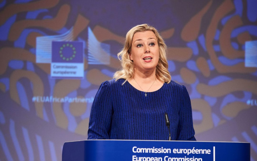 Vaaleahiuksisella naisella on tummansininen asu. Hän seisoo puhujapöntössä, jossa on teksti Comission européenne / European Comission.