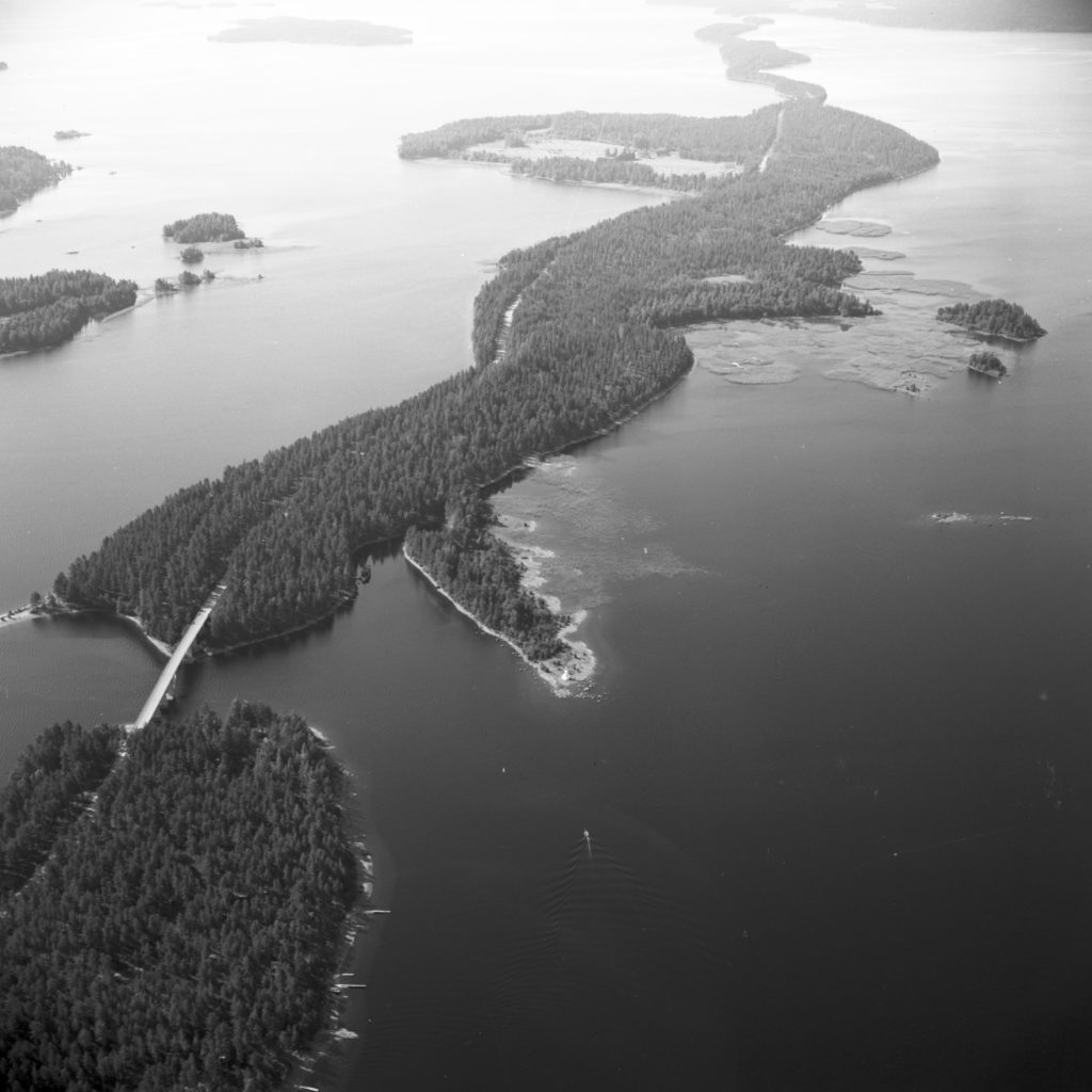 Mustavalkoinen ilmakuva. Järvessää kapeasta harjukaistaleesta muodostuneita saaria. Tie kulkee saarien läpi ja niiden välissä kulkevaa siltaa pitkin.
