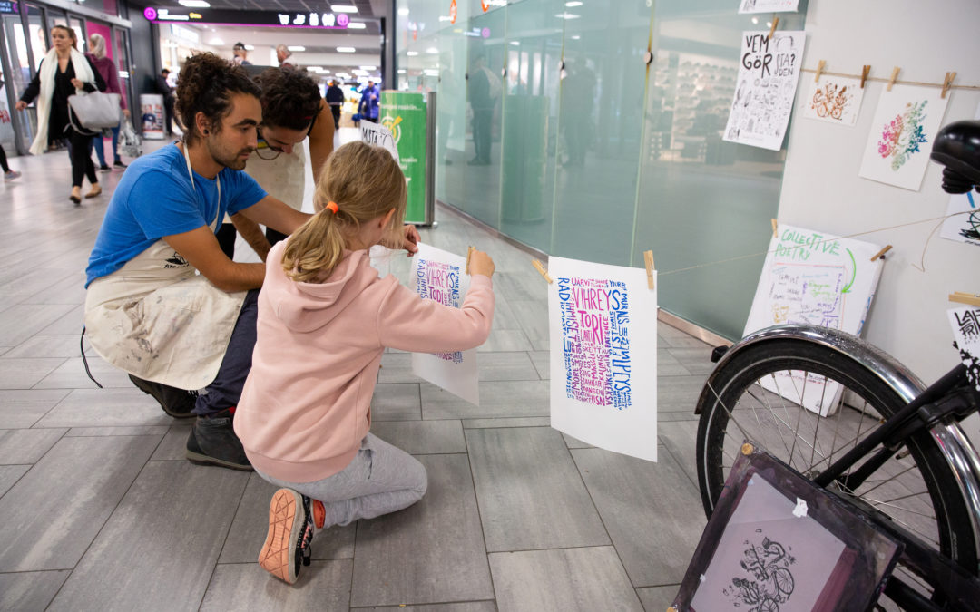 Aikuinen ja lapsi ripustamassa silkkipainettua kuvaa taidenäyttelyyn.