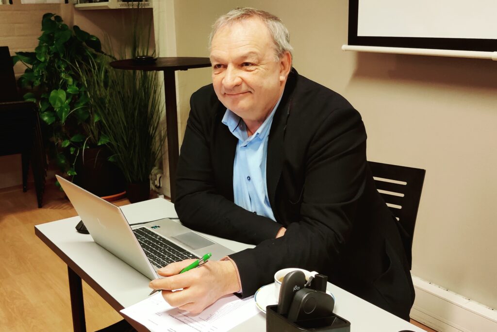 Kärkölän pormestari Markku Koskinen istuu kokouspöydän ääressä. Pöydällä hänen edessään on kannettava tietokone. Hänellä on kädessään kynä.